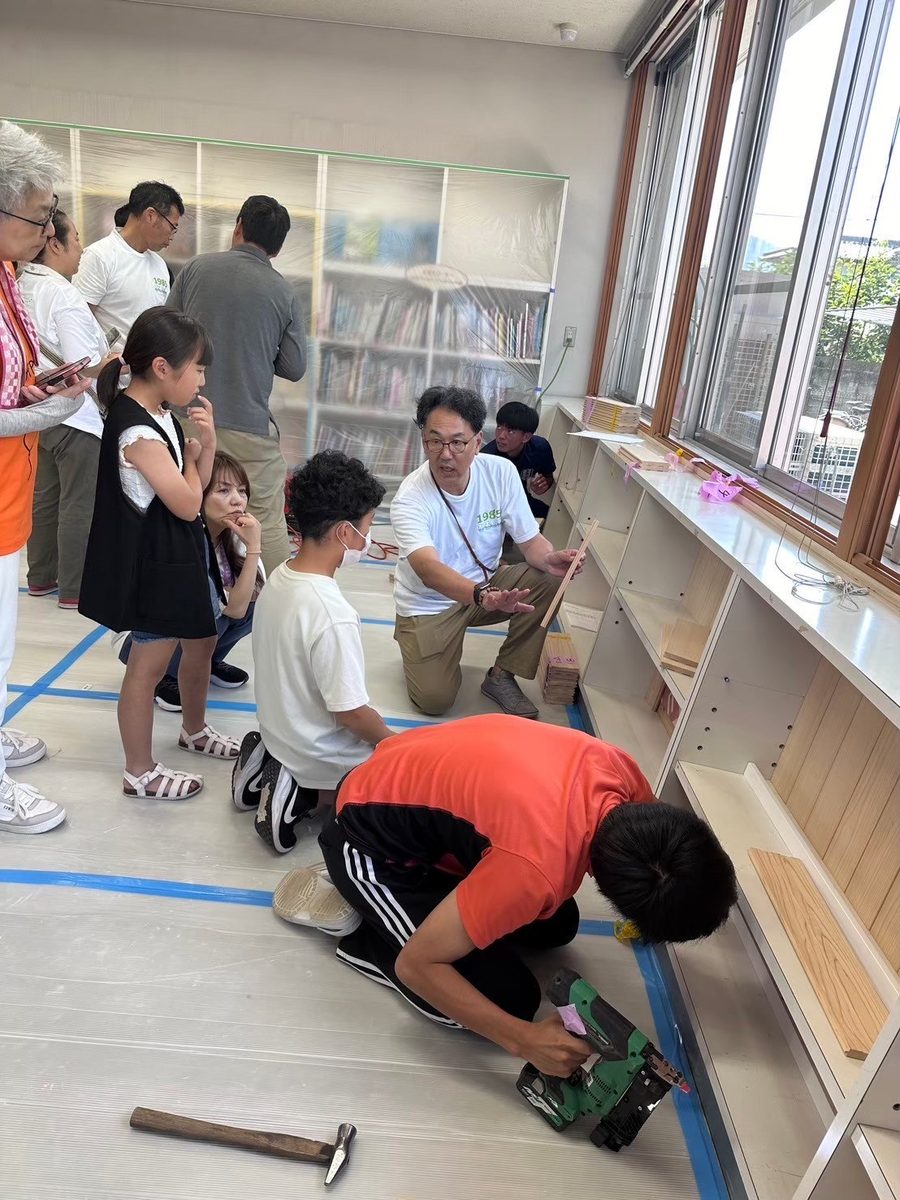 公民館の図書室で、子どもたちが大人に教わりながら電動工具で下地の木材を留めている様子。